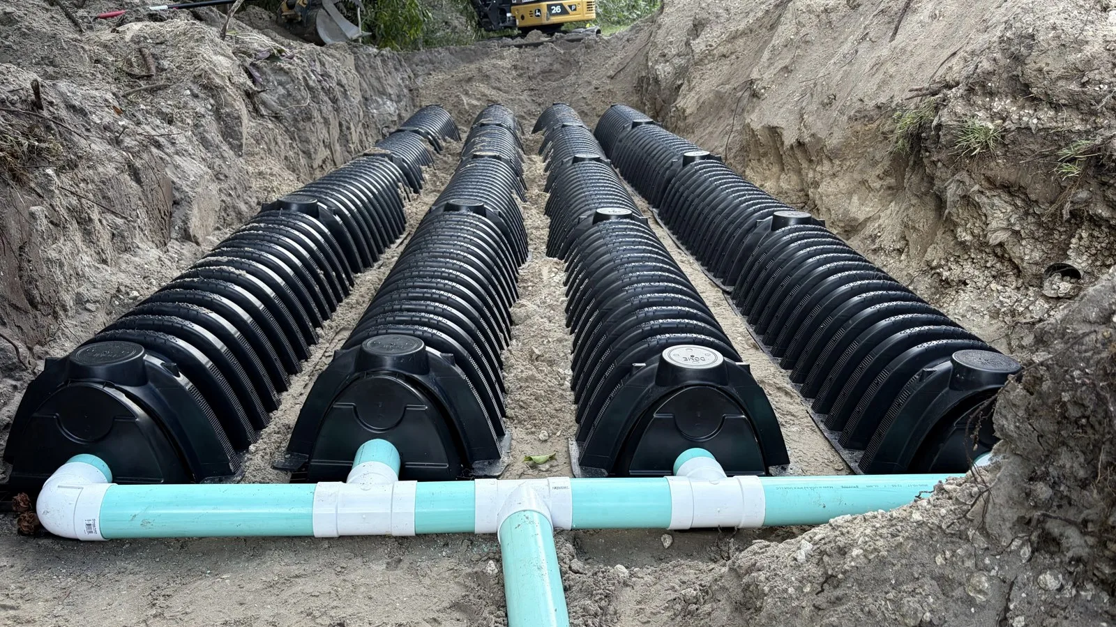 Four rows of plastic drain field chambers set in a sandy trench with the header pipe connected, during a new septic system installation in South Florida